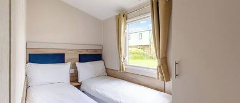 Un dormitorio con dos camas individuales, una ventana con cortinas y vistas al exterior.