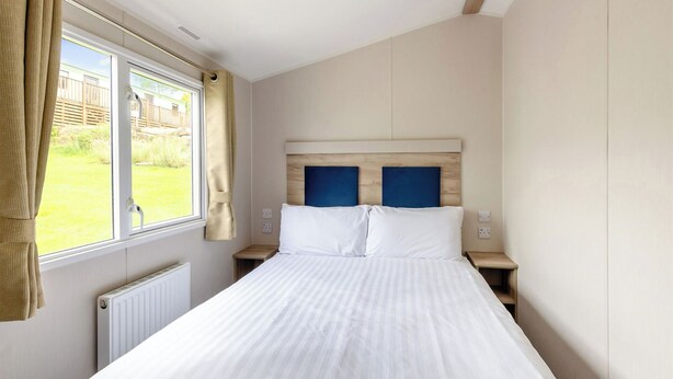 A bedroom with a bed, a window, a radiator, and a view of the outside. - Silver 3 Bedroom Caravan, Sleeps 8 P (Walton-on-the-Naze)