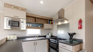 A modern kitchen with a microwave, toaster, sink, stove, and wooden cabinets. - Silver 3 Bedroom Caravan, Sleeps 8 P (Walton-on-the-Naze)
