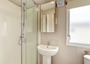 Un baño con cabina de ducha de vidrio, un lavabo blanco y una ventana.