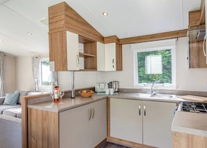 A compact kitchen with wooden cabinets, a built-in stove, and a window with a view of greenery.
