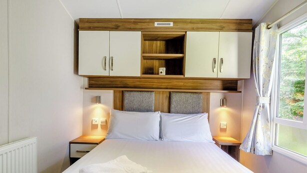Une chambre d’hôtel avec un lit, deux tables de chevet, une tête de lit en bois et une fenêtre avec des rideaux.