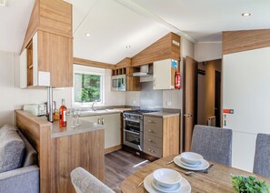 Cocina compacta con microondas, estufa y lavamanos, zona de comedor con mesa y sillas, y ventana con vistas a zonas verdes.