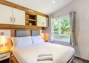 Una cama bien hecha con sábanas blancas, un cabecero de madera y una mesita de noche con una lámpara.