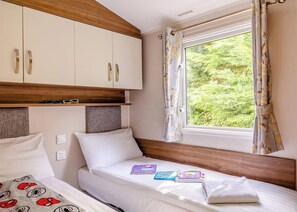 A bedroom with two beds, a window with curtains, and a wardrobe.