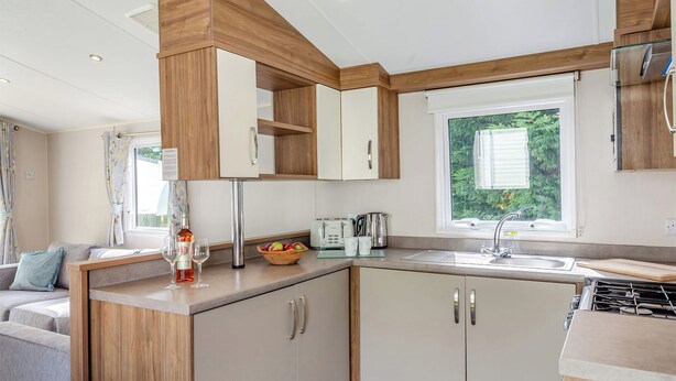 A compact kitchen with wooden cabinets, a built-in stove, and a window with a view of greenery. - Silver Premium 2 Bedroom Caravan, Sleeps 6 P (Walton-on-the-Naze)
