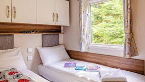 A bedroom with two beds, a window with curtains, and a wardrobe. - Silver Premium 2 Bedroom Caravan, Sleeps 6 P (Walton-on-the-Naze)