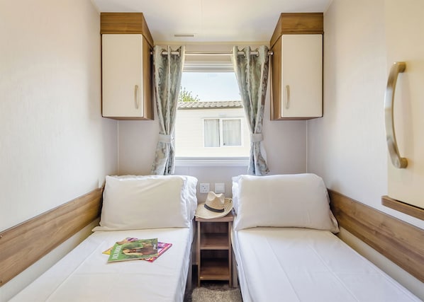 Une chambre à coucher de taille modeste, comprenant deux lits, une petite table et une fenêtre avec des rideaux.