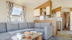 Un espacio de estar moderno con un sofá gris, una mesa de centro de madera y una cocina con armarios de madera y un microondas.