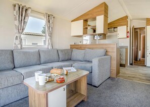 Un espace de vie moderne avec un canapé gris, une table basse en bois et un coin cuisine doté de meubles en bois et d’un four à micro-ondes.