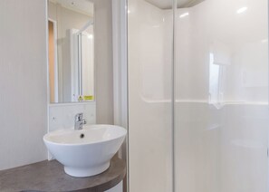 Un baño con lavamanos blanco, espejo y cabina de ducha con mampara de vidrio.