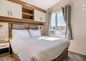 Un dormitorio con cama, cabecero de madera, armario empotrado, mesita de noche y ventana con cortinas.