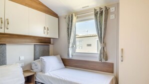 Un dormitorio con dos camas, cabeceros de madera, una ventana con cortinas y vistas a un edificio.