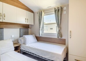 Une chambre avec deux lits, une tête de lit en bois, une fenêtre avec des rideaux et une vue sur un bâtiment à l’extérieur.