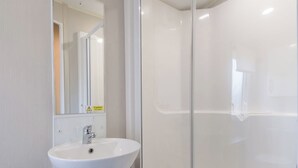 Ein Badezimmer mit einem weißen Waschbecken, einem Spiegel und einer Duschkabine aus Glas.