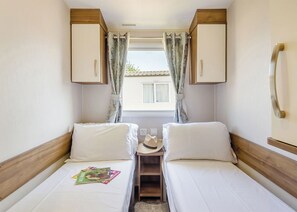 Una habitación pequeña y acogedora con dos camas, una mesita y una ventana con cortinas.