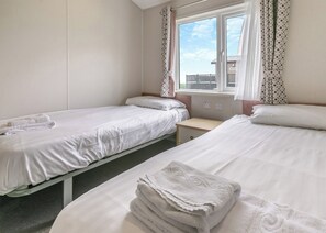 Une chambre d’hôtel avec deux lits simples, une petite table de chevet, une fenêtre avec des rideaux et une vue sur l’extérieur.