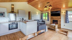 Eine moderne Küche mit Herd, Backofen und Mikrowelle, ein Essbereich mit Tisch und Stühlen, ein graues Sofa und ein an der Wand befestigter Fernseher.