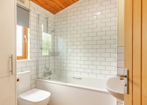 Ein Badezimmer mit weißen Fliesen, einer Badewanne, einer Toilette und einer Duschkabine.
