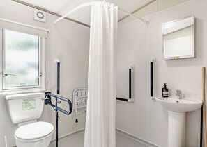 Un baño con inodoro, lavamanos, ducha con cortina, barra de apoyo y ventana.