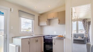 A compact kitchen with a stove, sink, and cabinets, a radiator, and a view of the outside. - Gold Accessible with parking P (Walton-on-the-Naze)