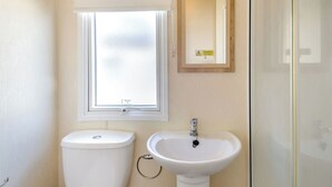 Une salle de bain comprenant des toilettes, un lavabo, une fenêtre avec du verre dépoli et un miroir orné d’un panneau d’avertissement.