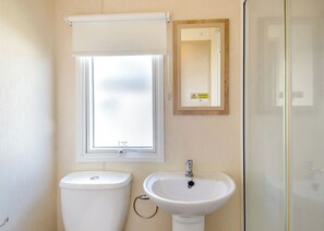 Ein Badezimmer mit Toilette, Waschbecken, einem Fenster mit Frostglas und einem Spiegel mit Warnhinweis.
