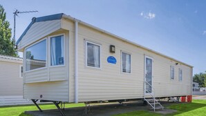 Une maison mobile équipée d’une rampe d’accès, d’une place de stationnement réservée et offrant une vue sur un ciel dégagé.
