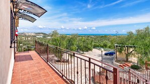Un balcón con vista al mar, un coche estacionado afuera y una pérgola con árboles.