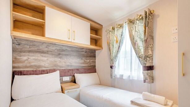 Une chambre d’hôtel avec deux lits, une tête de lit en bois, une petite étagère en bois et une fenêtre avec des rideaux.