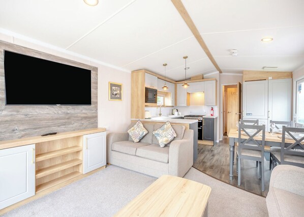 A compact living space with a TV, sofa, dining table, kitchen area, and a small island. - Gold Premium Caravan with decking & sea view (Ryde, Nr Bembridge)