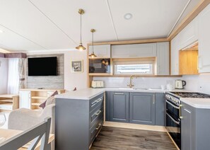 A modern kitchen with grey cabinets, a central island, a built-in oven, and pendant lighting. - Gold Premium Caravan, parking, ensuite, deck, SV 6 (Ryde, Nr Bembridge)