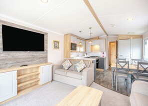 A compact living space with a TV, sofa, dining table, kitchen area, and a small island. - Gold Premium Caravan, parking, ensuite, deck, SV 6 (Ryde, Nr Bembridge)