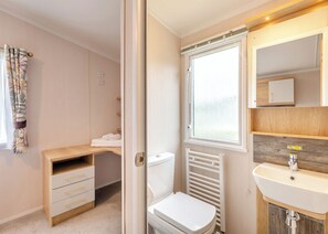 A compact bathroom with a toilet, a radiator, a sink, and a window. - Gold Premium Caravan with ensuite & decking (Ryde, Nr Bembridge)