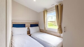 Quarto com duas camas, janela com cortinas, cabeceira de madeira e interruptor de luz na parede.