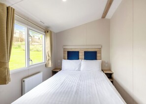 Une chambre à coucher avec un lit, une fenêtre avec des rideaux, un radiateur et une vue sur l’extérieur.