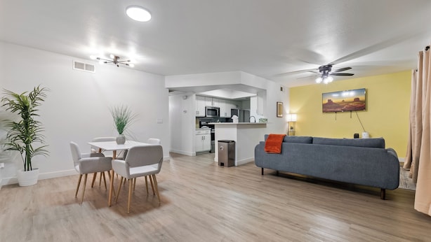 A modern living room with a gray sofa, a dining table with chairs, a kitchen area, and a ceiling fan. - Great for Mid/Long Stays - Pool - King Bed (Mesa)