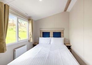 A bedroom with a bed, a window with curtains, a radiator, and a view of the outside. - Silver Caravan with decking (Ryde, Nr Bembridge)
