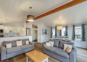 A modern living room with two sofas, a wooden coffee table, and a kitchen in the background. - Deluxe Lodge with parking, ensuite & decking 4 P (Ryde, Nr Bembridge)