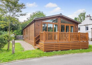 A wooden cabin with a balcony, a staircase, and a brick pathway leading to the entrance. - Deluxe Lodge with parking, ensuite & decking 4 P (Ryde, Nr Bembridge)