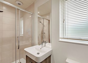 Ein modernes Badezimmer mit einer gläsernen Dusche, einem weißen Waschbecken und einem Fenster mit Jalousien.