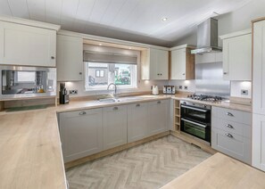 A modern kitchen with a herringbone floor pattern, stainless steel appliances, and a window with blinds.