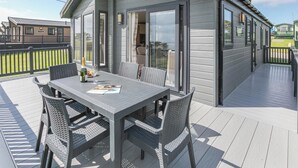 A deck with a table and chairs, a bottle of champagne, and a glass. - Deluxe Lodge, parking, ensuite, decking & sea view (Ryde, Nr Bembridge)