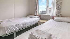 Camera d'albergo con due letti singoli, un comodino, una finestra con tende e vista sull'esterno.
