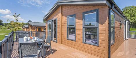 A wooden cabin with a deck, a table with chairs, and a view of the surrounding landscape.