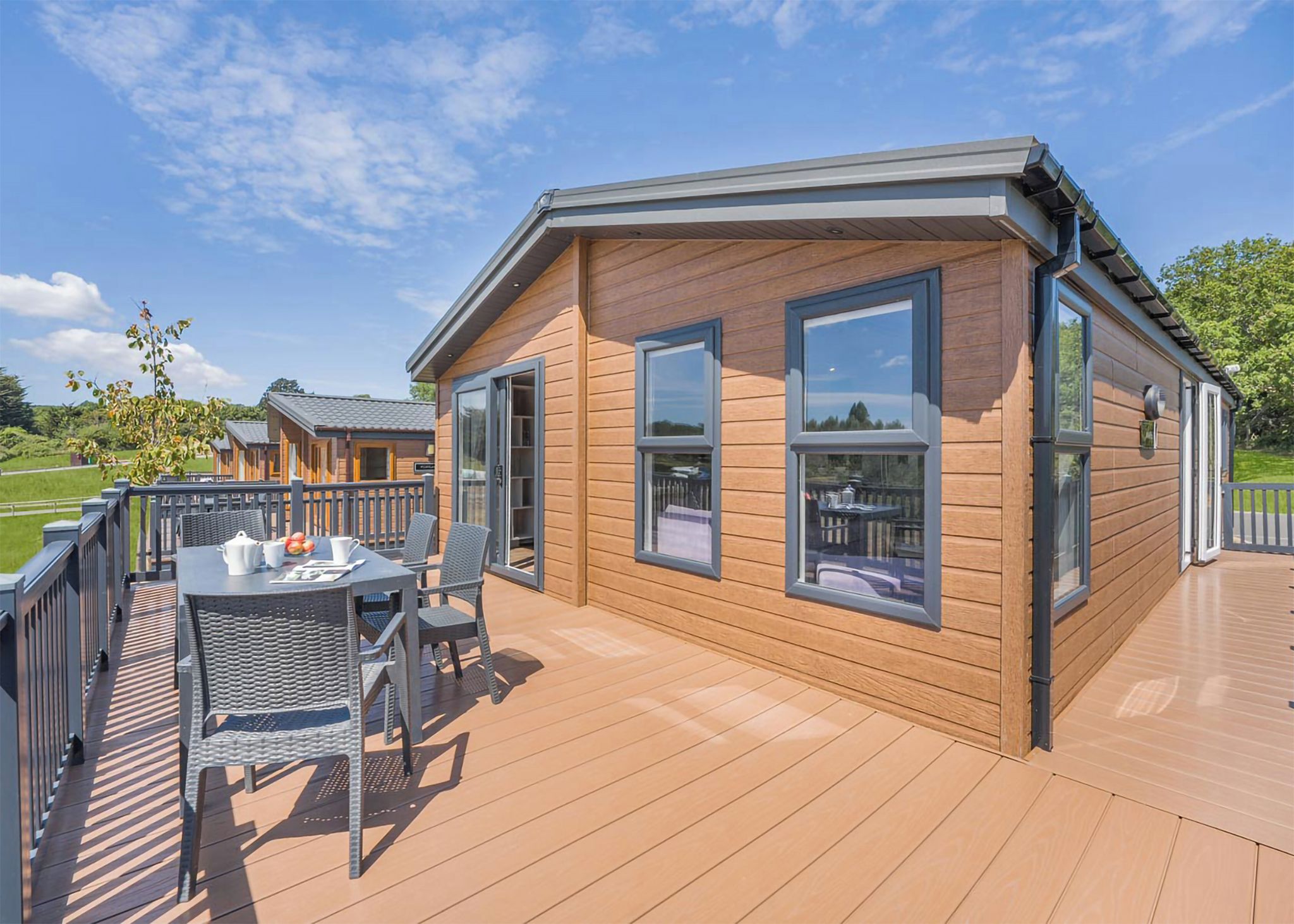 En træhytte med en terrasse, et bord med stole og udsigt over det omkringliggende landskab.