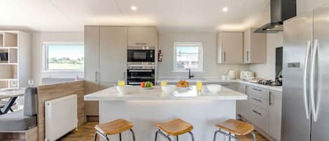 Una cocina moderna con una isla central, taburetes de bar, electrodomésticos de acero inoxidable y vistas al exterior.