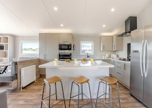 A modern kitchen with a central island, bar stools, stainless steel appliances, and a view of the outdoors. - Prestige Lodge with parking, ensuite & decking 4 (Ryde, Nr Bembridge)