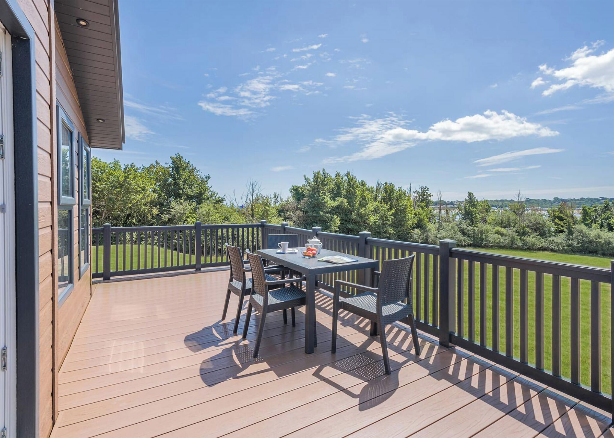 A deck with a table and chairs, overlooking a grassy area and trees.