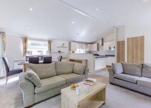 A modern living room with a sofa, a coffee table, and a dining area with chairs and a table. - Prestige Lodge, parking, ensuite, decking & SV 6 (Ryde, Nr Bembridge)